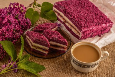 Kadınsı aksesuarlı yaratıcı kompozisyon, güzel leylak çiçekleri, kahve ve badem kurabiyeleri. Mor Taro keki.