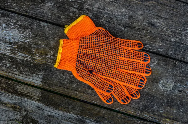 Turuncu iş eldivenleri bahçedeki ahşap bir tahtanın üzerinde yatıyor. .