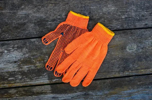 Turuncu iş eldivenleri bahçedeki ahşap bir tahtanın üzerinde yatıyor. .