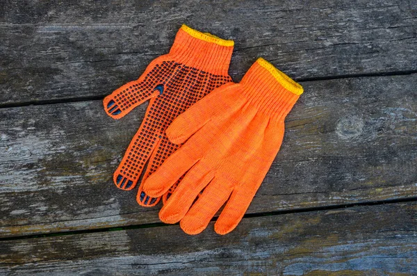 Turuncu iş eldivenleri bahçedeki ahşap bir tahtanın üzerinde yatıyor. .