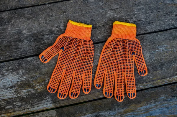 Turuncu iş eldivenleri bahçedeki ahşap bir tahtanın üzerinde yatıyor. .