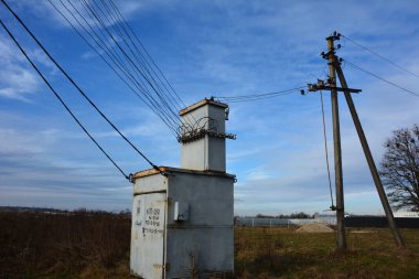Kırsal kesimde eski bir trafo kulübesi ve elektrik direkleri. Kablolar ve beton sütunlarla çevrili trafo kulübesi.