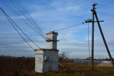 Kırsal kesimde eski bir trafo kulübesi ve elektrik direkleri. Kablolar ve beton sütunlarla çevrili trafo kulübesi.