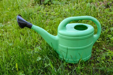 Bahçe bitkilerini sulamak için büyük yeşil bir plastik sulama kutusu yeşil bir çimenlikte duruyor. Yazın bahçıvanlık. W Plastik sulama kabı yabani kekikler arasında yeşillik üzerinde.