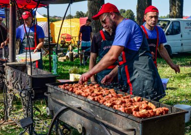 Lviv.Ukrayna. Mayıs 2021. Şef ızgarada et kızartıyor. Siyah önlüklü aşçı eti ateşte kızartıyor. Açık havada barbekü. Parlak bokeh.