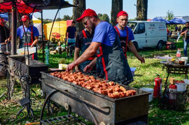 Lviv.Ukrayna. Mayıs 2021. Şef ızgarada et kızartıyor. Siyah önlüklü aşçı eti ateşte kızartıyor. Açık havada barbekü. Parlak bokeh.