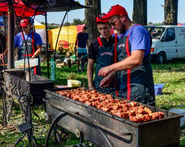 Lviv.Ukrayna. Mayıs 2021. Şef ızgarada et kızartıyor. Siyah önlüklü aşçı eti ateşte kızartıyor. Açık havada barbekü. Parlak bokeh.