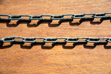 Gri parlak bir zincirin pek çok örneği. Yeni bir metal zincir ahşap bir masanın üzerinde yatıyor..