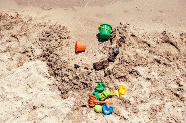 Renkli plastik oyuncaklar: Sarı kürek, yeşil ve kırmızı küfler deniz kenarındaki kumsalda yatıyor. Arka planda hareket eden küçük dalgalar. Deniz kıyısında oynayan çocuklarla yaz tatili kavramı