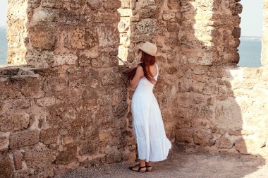 Bu fotoğraf, beyaz elbiseli güzel kızıl saçlı turist bir kızın antik şehirde kale duvarının en üstünde poz vermesini tasvir ediyor..