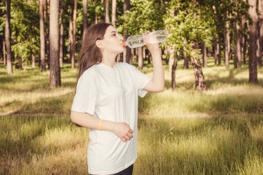 Bu fotoğraf, bahçedeki dinlenme, dinlenme ve tren eğitimlerinden sonra şişeden su içen genç ve güzel bir kızın görüntüsünü gösteriyor..