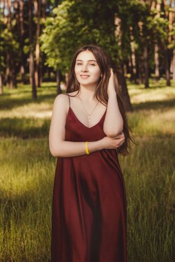 Bu fotoğraf, bordo elbiseli hoş bir kızın doğal bir parkta yürüyüşünü, açık hava bahçesinde gülümsemesini gösteriyor..