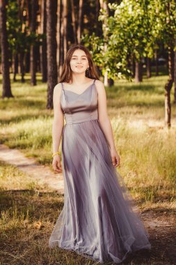 Bu fotoğraf, gri kabarık elbiseli hoş bir kızın doğal bir parkta yürüyüşünü, açık hava bahçesinde gülümsemesini gösteriyor..