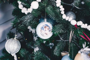 Bu fotoğraf Noel süslemelerini tasvir ediyor. Parlayan ampuller. Tatil için süslenmiş Noel baloları. Çok renkli aksesuarlar. Noel ağacının dalları çelenklerle süslenmiştir..