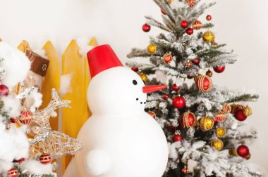 Bu fotoğraf, Noel ağacının yakınındaki büyük bir yapay kardan adamı sarı bir çitin arkasında tasvir ediyor..