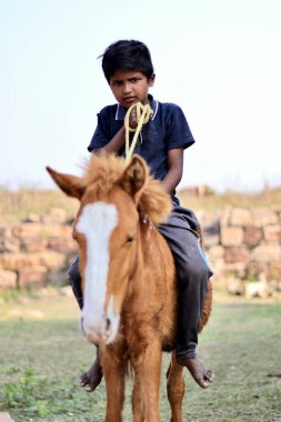 Belgaum, Karnataka, Hindistan - 25 Aralık 2021: At süren genç bir Güney Hintli çocuğun (çiftçinin oğlu) seçici odak noktası.