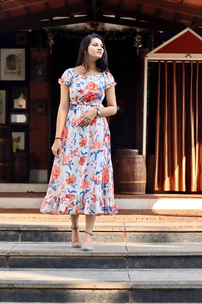 An Indian young woman or lady in floral one piece dress coming out of a club.