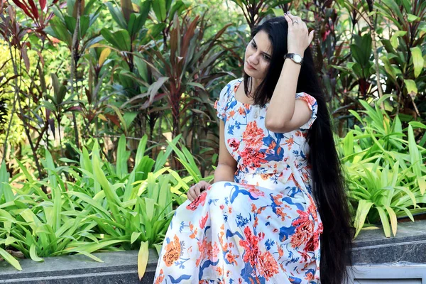 An Indian young woman or lady in floral one piece dress relaxing in a garden.