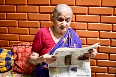 Davangere, Karnataka, Hindistan - 18 Mart 2021: Bir evin yastığında oturan ve Kannada dilinde gazete okuyan çok yaşlı bir Güney Hintli kadının güzel bir portresi.