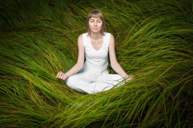 Yeşil çimenlerin üzerinde oturan ve meditasyon sarışın kız.