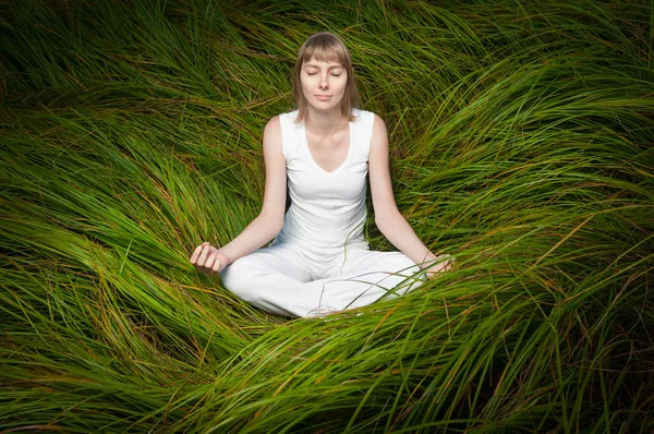 緑の芝生の上に座って、瞑想のブロンドの女の子. — ストック写真