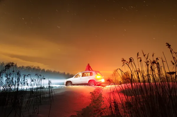 Noche de invierno con nieve y coche con faros encendidos . — Foto de Stock