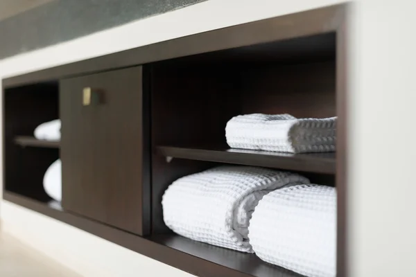 Witte towels handdoeken gerold op plank in hotel badkamer. Stockafbeelding