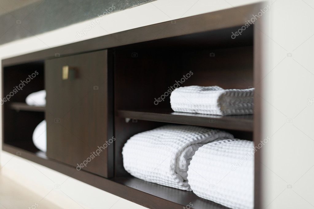 Rolled white towels on shelf in hotel bathroom.