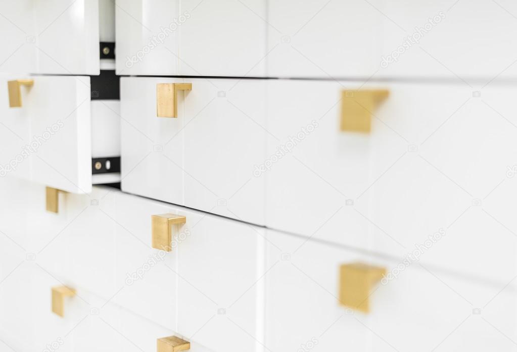 White sleek drawers with golden handles.