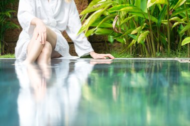 ayakları suda havuz başında oturan kadın.