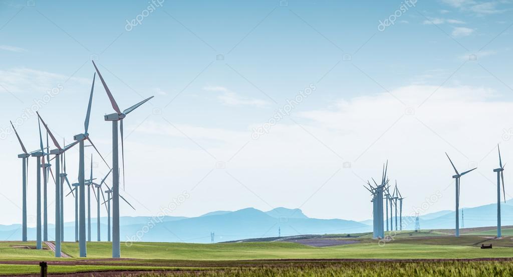 Wind turbines on green field over blue sky.