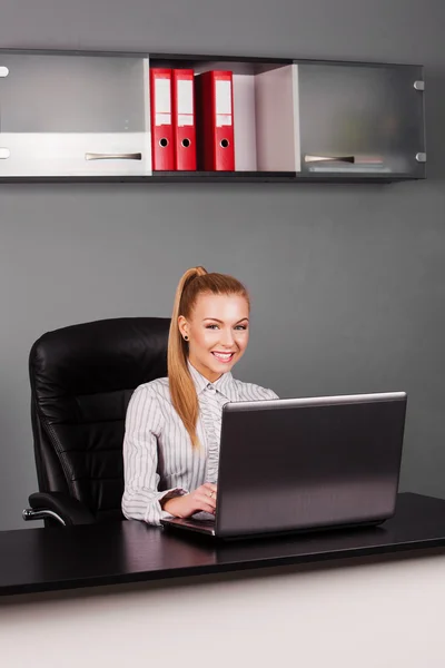 Счастливая улыбающаяся деловая женщина, печатающая на ноутбуке за своим столом — стоковое фото