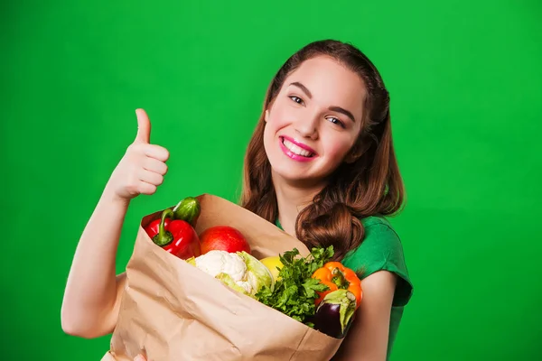 Szép boldog nő gazdaság egy élelmiszerbolt táskányi friss és egészséges élelmiszer. zöld háttér — Stock Fotó
