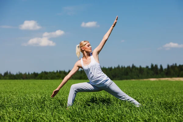 Молодая блондинка делает упражнения йоги на зеленой траве. Концепция йоги . — стоковое фото