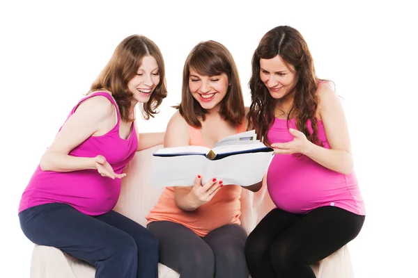 Улыбающиеся счастливые беременные женщины сидят и читают книгу — стоковое фото