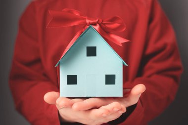 Elinde hediye kurdelesi olan bir evin kağıt modeli.