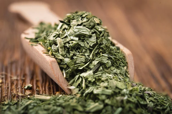 Crushed dried basil leaves in a wooden scoop