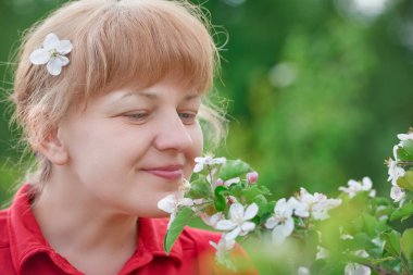 Orta yaşlı bir kadın ve bahçede çiçek açan bir ağacın dalları.