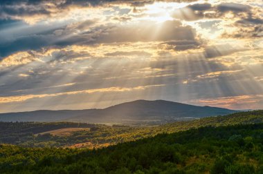 Güneşin ışınları fırtına bulutları arasında dağlık ormanlarda dramatik bir şekilde dağılıyor.