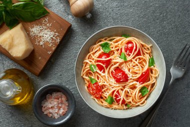 Plate of spaghetti with cherry tomatoes and fresh basil and ingredients on grey background top view