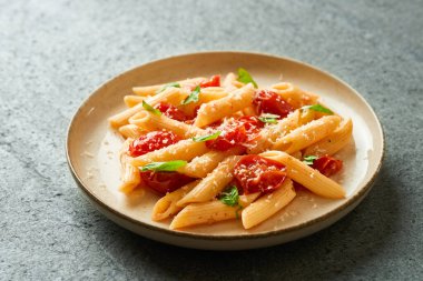 Penne pasta with cherry tomatoes on gray background high angle closeup indoors