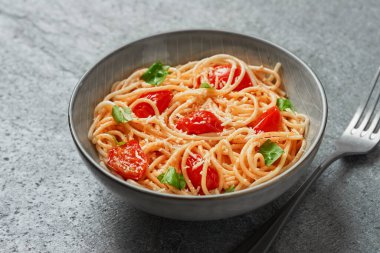 Spaghetti with cherry tomatoes and basil close-up on grey background from a high angle view indoors