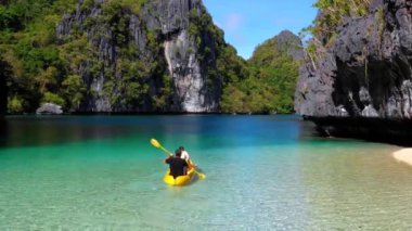 Couple doing kayak in the middle of the Big Lagoon of El Nido, Philippines. Perfect leisure for travel and paradise summer holidays under the sun - aerial view with a drone 4K