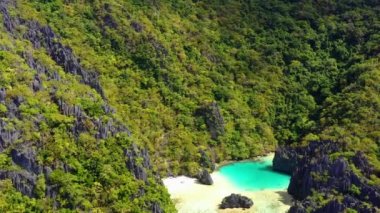 Turquoise lagoon surrounded by mountains and trees in El Nido, Philipplnes. Beautiful landscape in paradise, perfect for travel in nature under the sun - Aerial view with a drone 4K