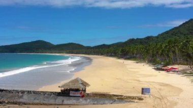 Beach of El Nido with lifeguard post in the front, Philippines. We can see mountains and palm trees forest in the background next to the white-sand - aerial view with a drone 4K