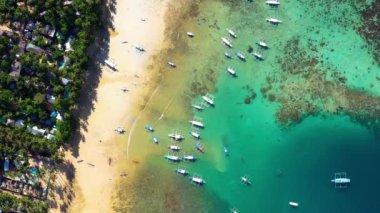 Boats on El Nido beach, Philippines. There is people on the sand near house in the middle of palm trees, perfect for summer holidays - aerial view with a drone 4K