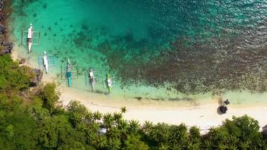 Aerial view over boats on El Nido beach, Philippines. Water is clear and turquoise near sand and palm trees, perfect for leisure activity in summer holidays 4K