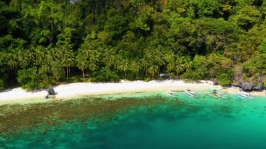 Aerial view over boats on El Nido beach, Philippines. Water is clear and turquoise near sand and palm trees, perfect for leisure activity in summer holidays 4K