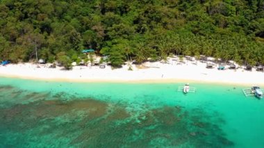 Boats on El Nido beach, Philippines. There is people on the sand in the middle of nature and palm trees, perfect for summer travel - aerial view with a drone 4K