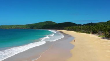 Couple on the beach with white-sand of El Nido, Philippines. We can see mountains and palm trees forest in the background, perfect for summer travel in nature - aerial view with a drone 4K